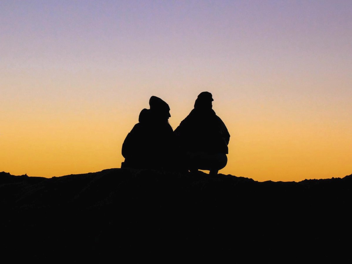 Deux personnes assises côte à côte au coucher du soleil